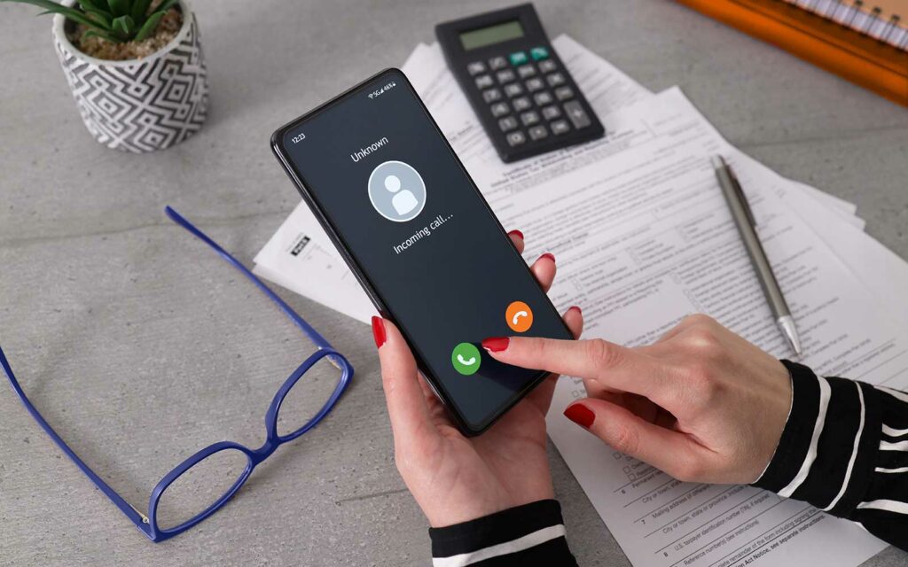 A stock image example of a woman holding a phone and wavering on her decision to answer a call from an unknown number